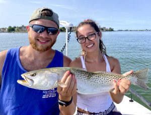 A girl holds up a healthy seatrout next to her boyfriend on the bow of a boat