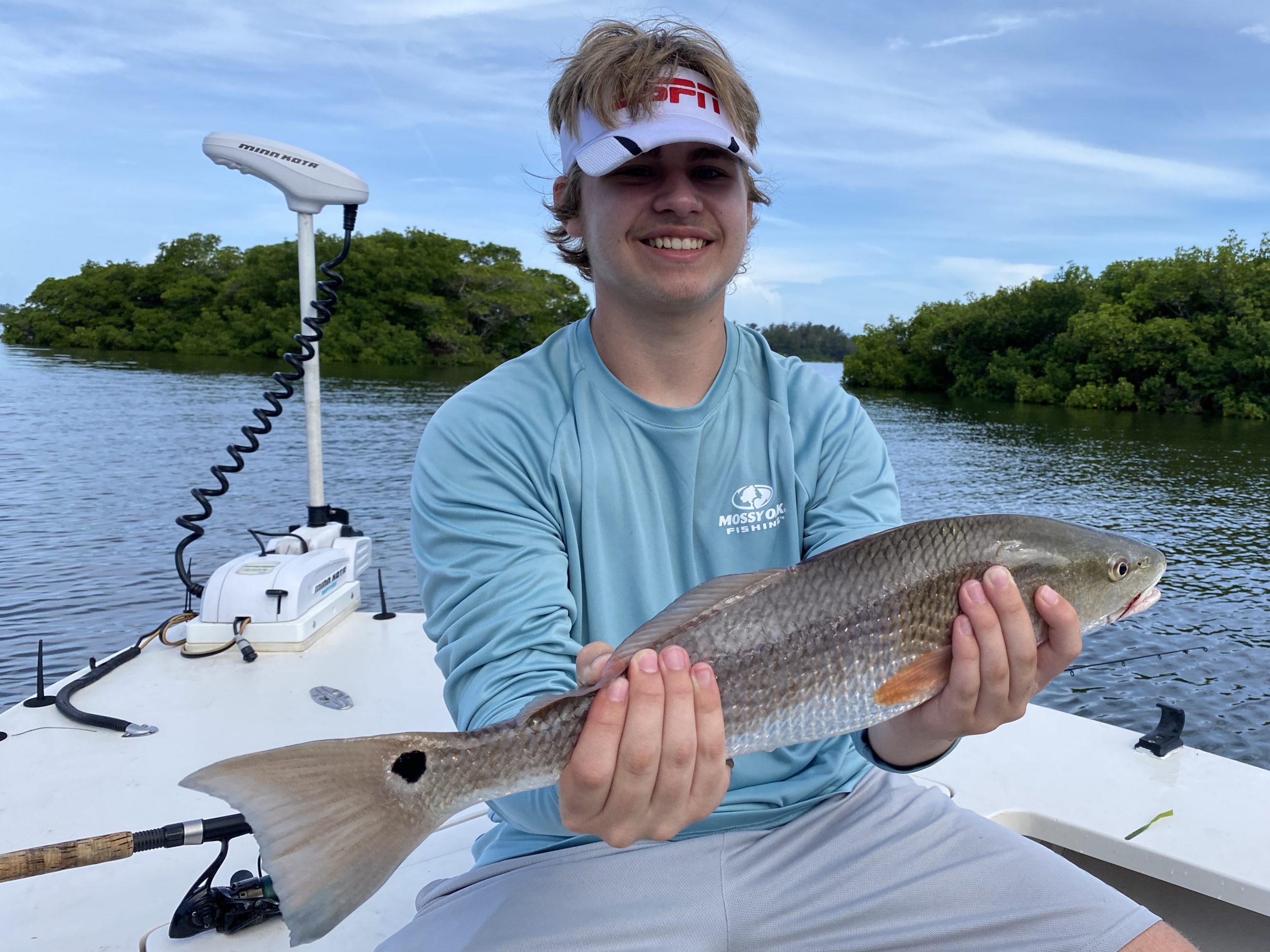 A young mustached angler holds a redfish for the camera. Mangrove islands dot the background of this picture