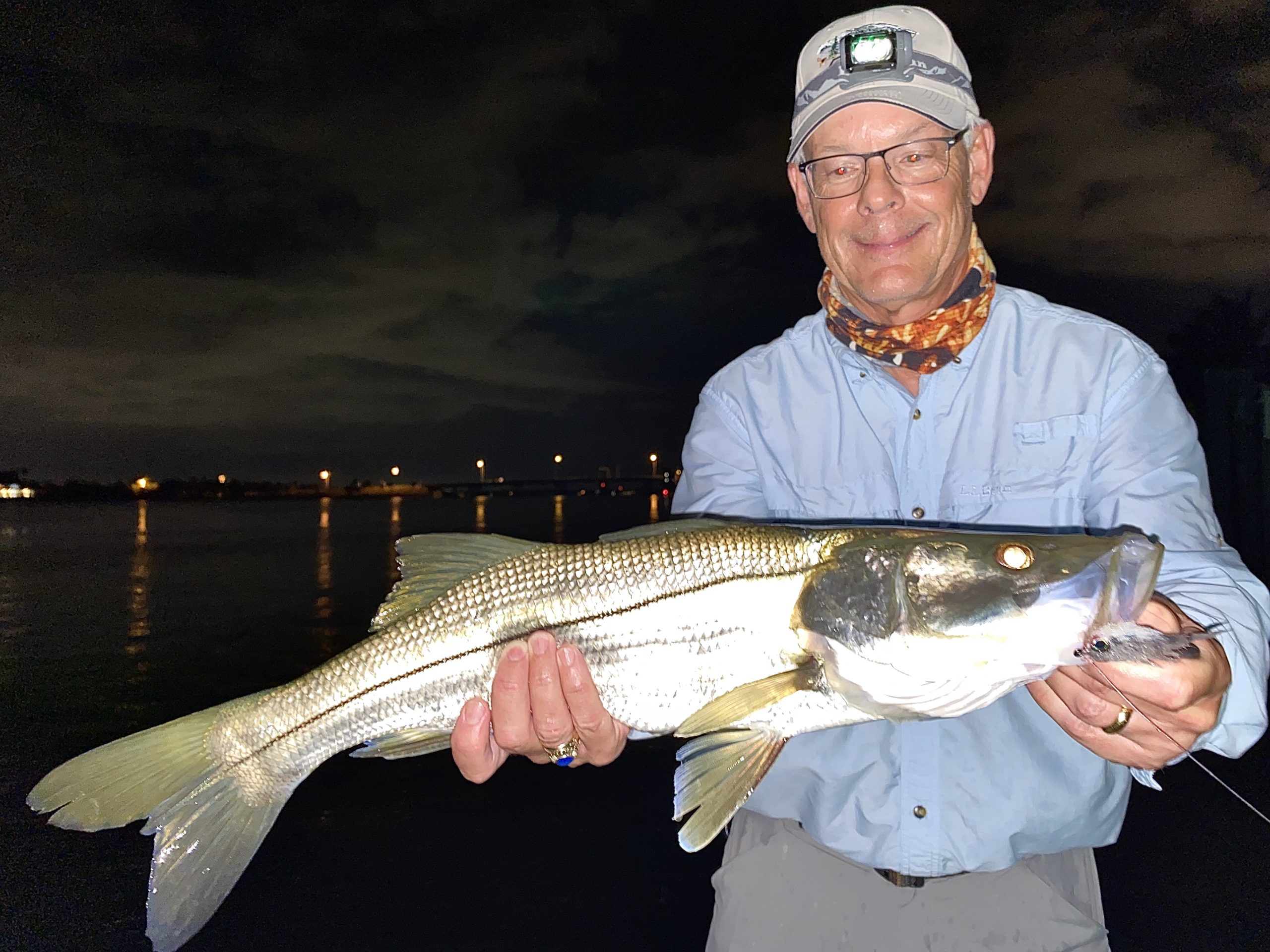 An angler holds a snook up for the camera at night