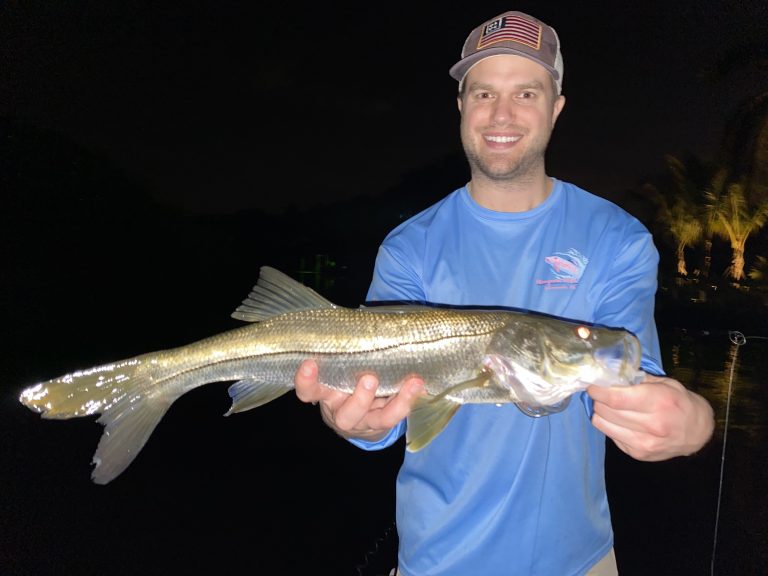 An angler holds a snook caught while fly fishing dock lights in FLorida