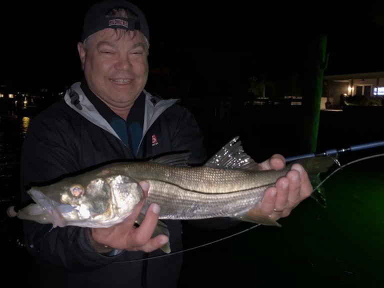 An angler holds a snook caught at night