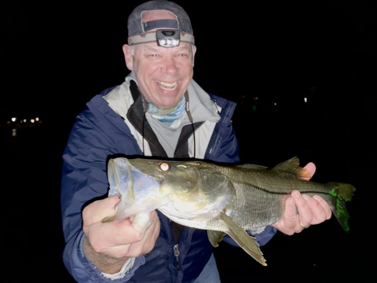 An angler smiles after catching a snook on the fly in dock lights