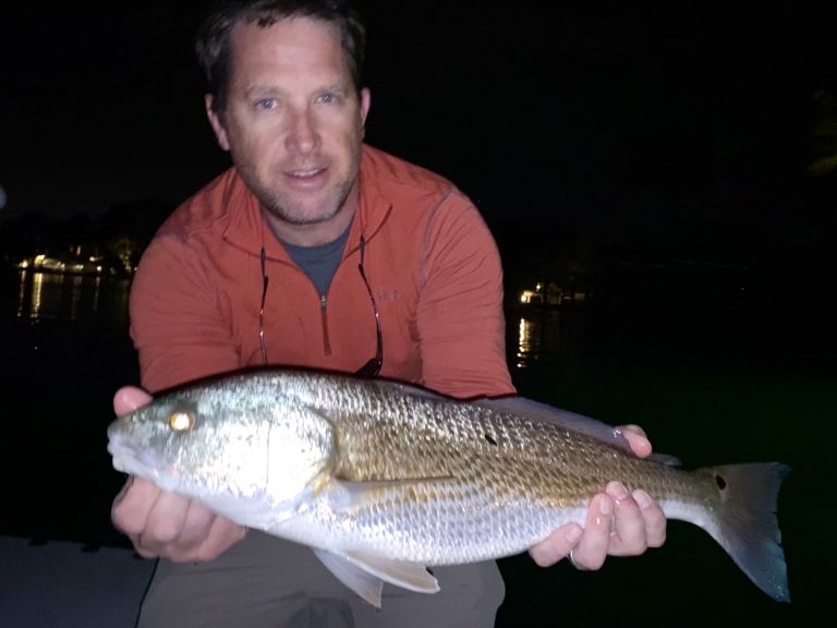 An angler holds a redfish caught on the dock lights up to the camera