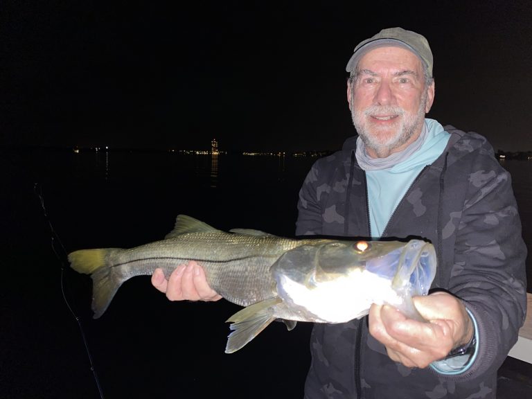 An angler holds a snook up for the camera caught on the dock lights at night