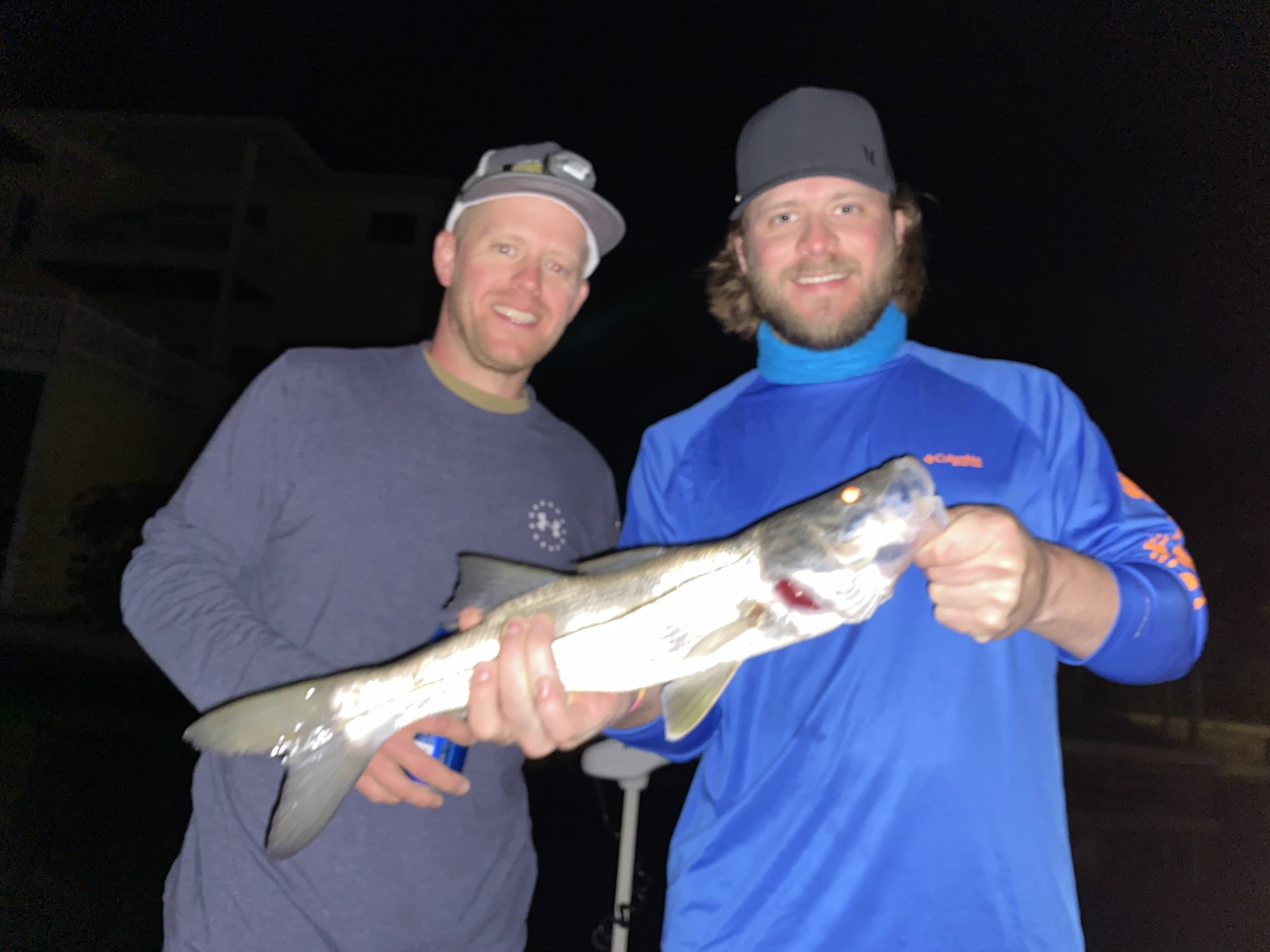 Two anglers hold a snook they caught while fishing dock lights on a fishing charter in Sarasota, FL