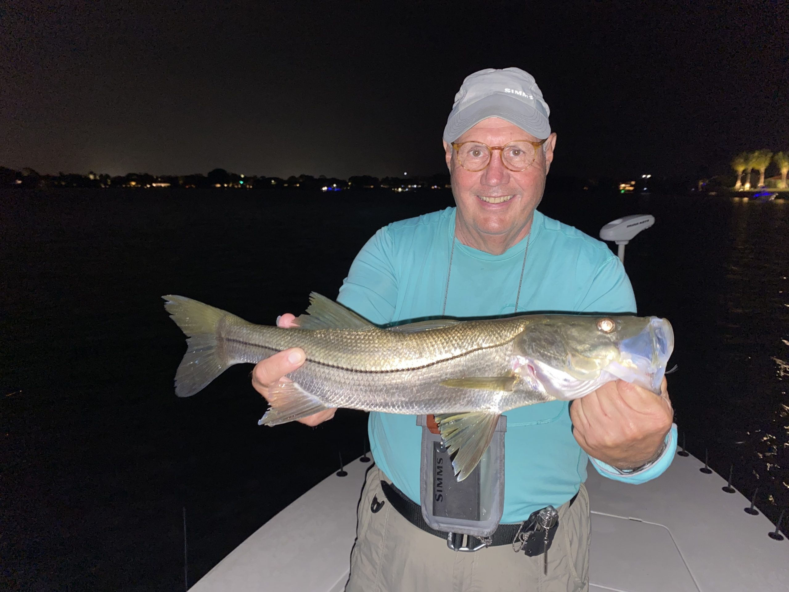 An angler holds a snook that he caught while fly fishing at night in snook alley