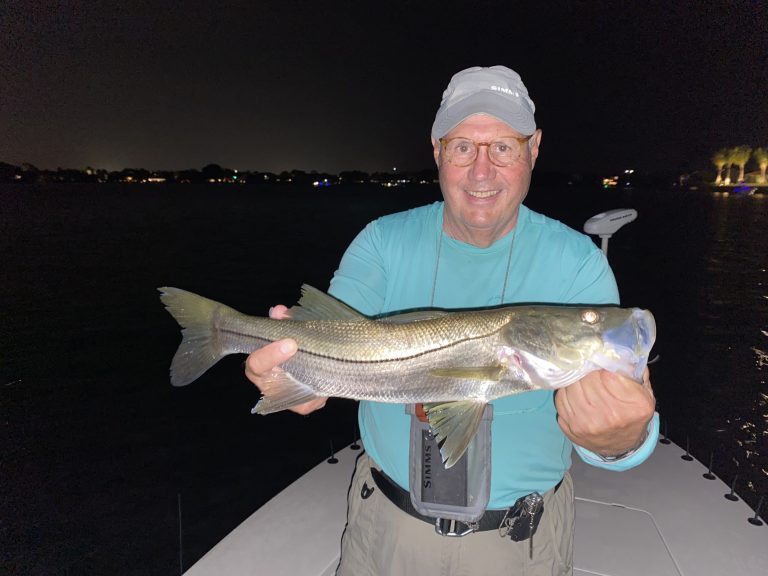 An angler holds a snook he caught while dock light fishing