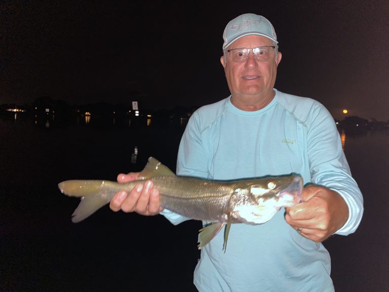 An angler holds a snook he caught while fly fishing for snook on dock lights
