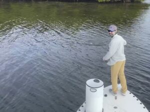 a fly angler smiles back at the camera as he fights a redfish