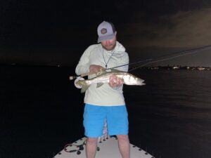 An angler poses with a snook that he caught while fly fishing the dock lights