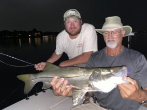 Two anglers smile as they hold a healthy snook they caught