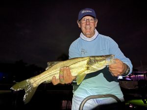 An angler holds a snook that he caught while fly fishing at night