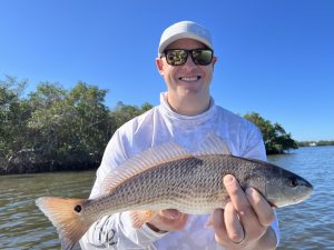 an angler smiles to the camera as he holds a redfish that he caught