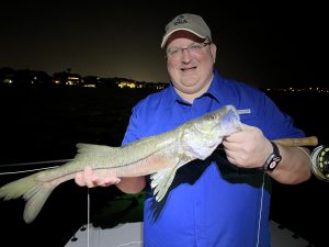 an angler holds a snook that he caught while fly fishing at night