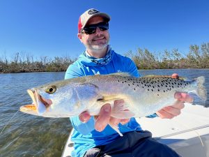 An angler holds a speckled seatrout the he caught while fly fishing