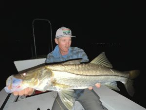 An angler holds a giant snook caught while fly fishing at night
