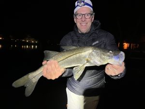 An angler holds up a snook that was caught while fly fishing at night