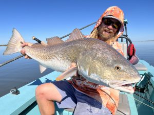 An angler smiles while posing with a giant redfish caught in the Louisiana marsh
