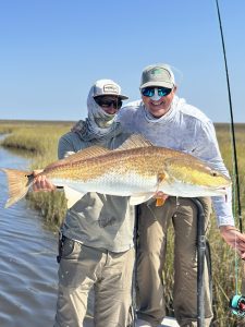 A guide stands next to an angler holding up a redfish for the camera. It's a big refish caught in a narrow creek