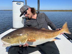 An angler smiles and admires the giant redfish that he caught while fly fishing