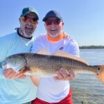 Two anglers hold a redfish up for the camera