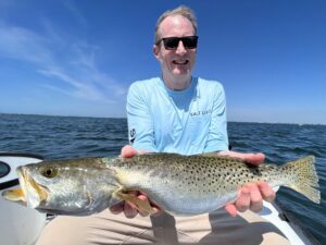 an angler holds a speckled seatrout up to the camera. This is a larger than average fish with a nice belly