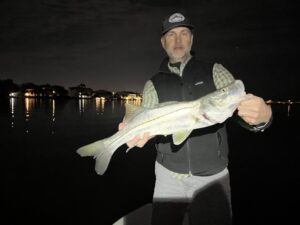 An angler holds a snook that was caught at night with a fly rod