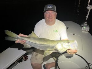 An angler holds a snook caught while fly fishing dock lights