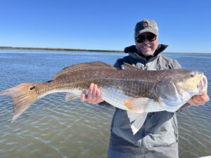 An angler smiles while holding a giant bull redfish