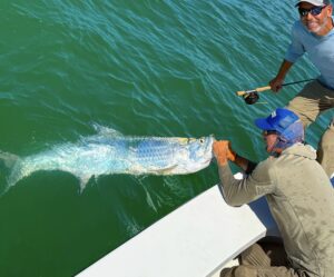 A fishing guide grabs a tarpon along side the boat as the angler smiles