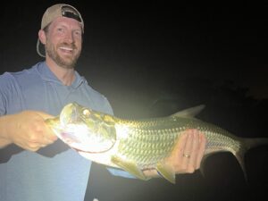An angler smiles while he holds a juvenile tarpon at night in Sarasota, FL
