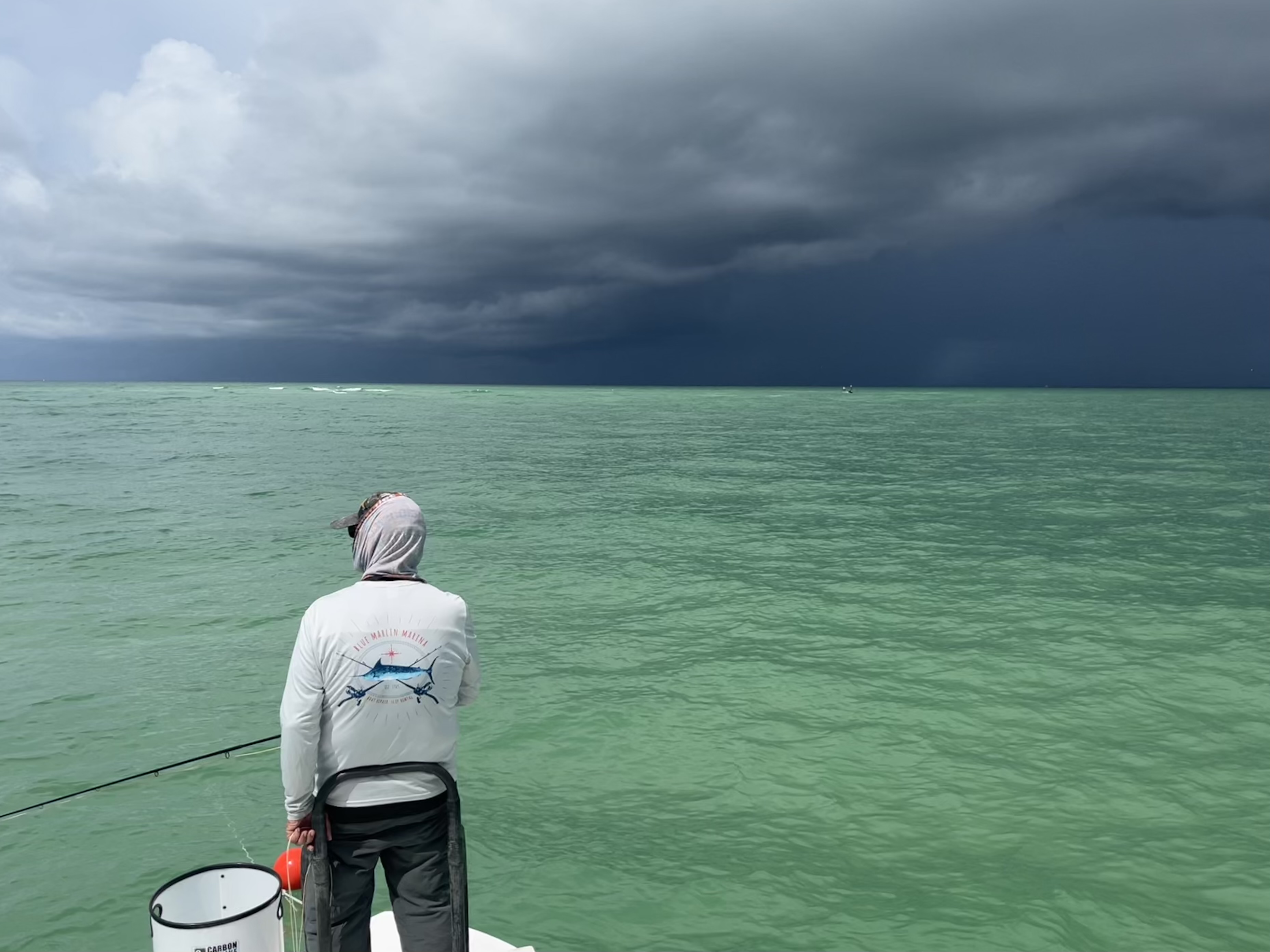 An angler stands on the bow of a skiff as a dark cloud approaches