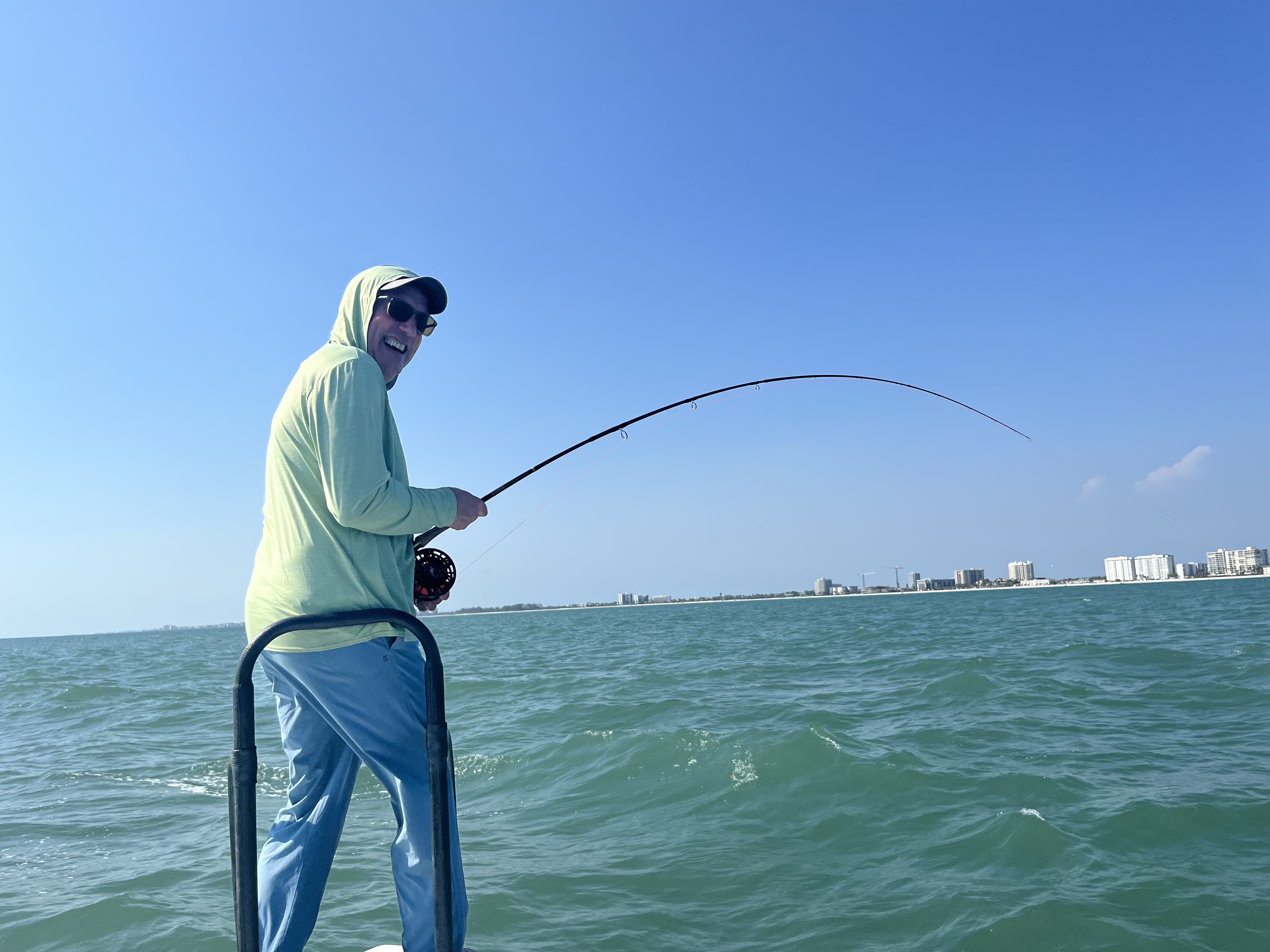 A happy angler stands on the bow of a boat and fights a tarpon