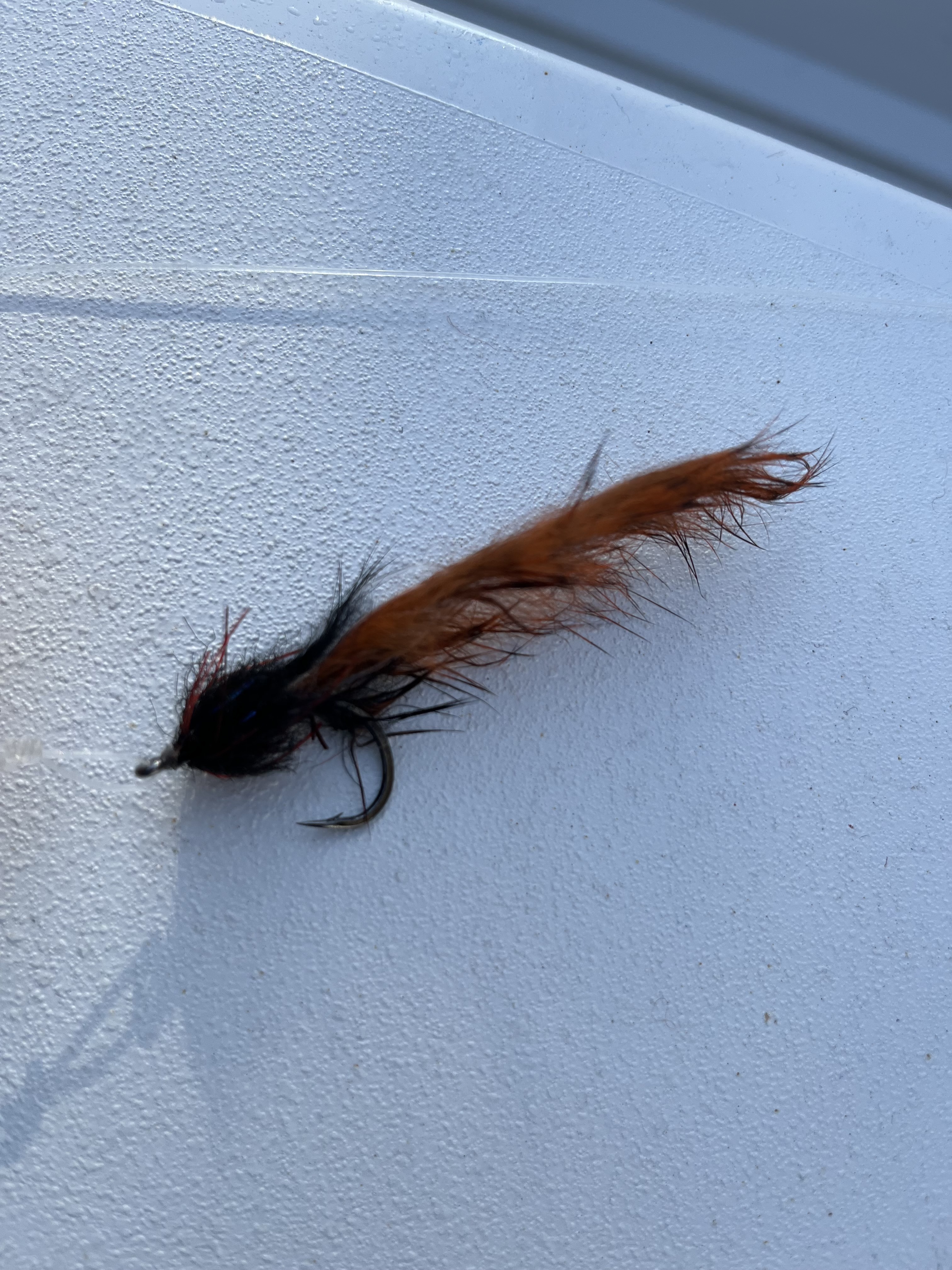 A fly used to catch tarpon laying on the deck of a boat. It's orange and black in color